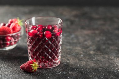Kırmızı böğürtlenlerden gelen yaz ferahlatıcı içecek kavramı: taze çilek ve kızılcık morsu siyah arka planda susuzluğunuzu gidermek için harika bir içecektir. Yatay yönelim.