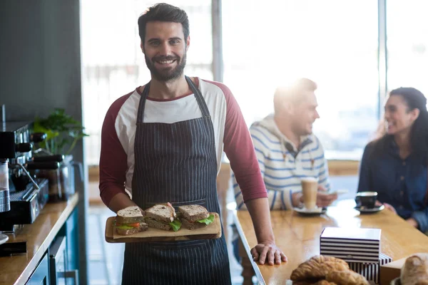 Camarero sosteniendo un sándwich en la tabla de cortar — Foto de Stock