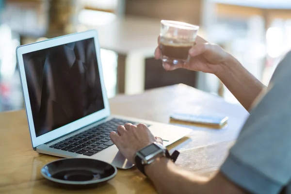 Uomo che utilizza un computer portatile mentre prende un caffè — Foto Stock