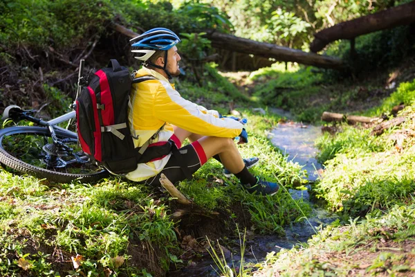 Mountain biker siedzi w pobliżu strumienia — Zdjęcie stockowe