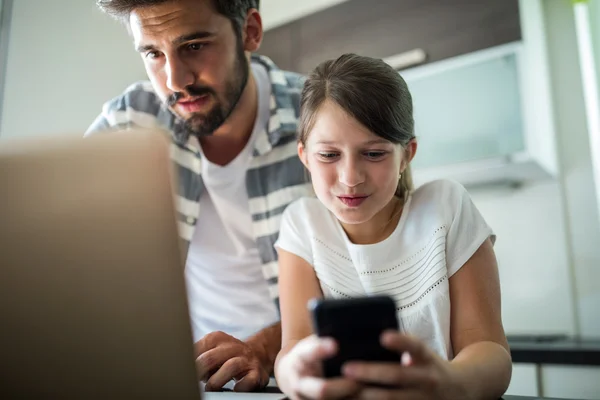 Father and daughter using laptop and mobile phone in the living room — Stockfoto