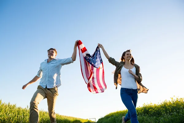 Pareja sosteniendo bandera de Amrican y corriendo en el campo — Foto de Stock