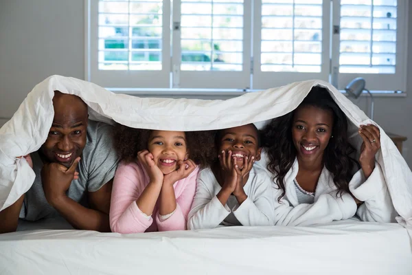 Família deitada debaixo de um cobertor na cama — Fotografia de Stock