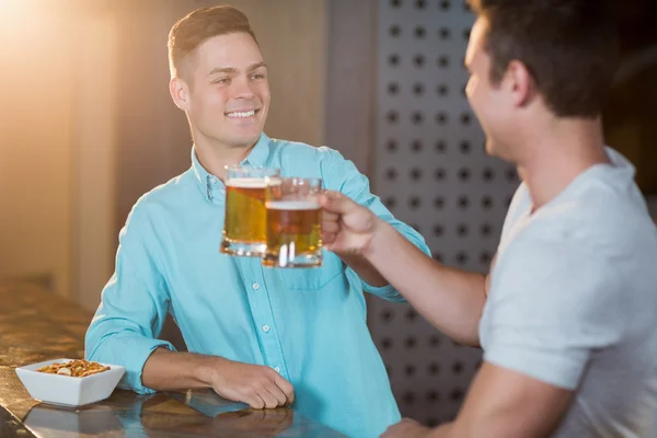 Amigos torrando canecas de cerveja no balcão do bar — Fotografia de Stock
