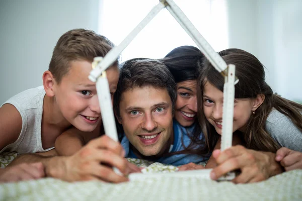 Family playing with model house in bedroom — Stockfoto