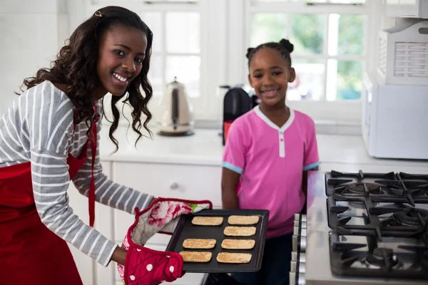 Mother putting baking tray in oven — Stock Photo, Image