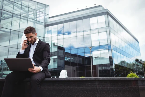 Affärsman med laptop medan du talar i telefon — Stockfoto