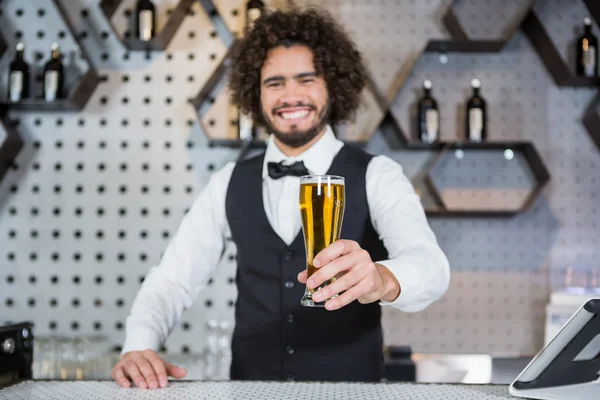 Cantinero sosteniendo vaso de cerveza en el mostrador del bar — Foto de Stock