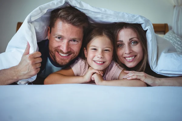 Família deitada debaixo de um cobertor na cama — Fotografia de Stock