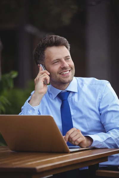 Uomo d'affari che parla al telefono mentre utilizza il computer portatile — Foto Stock