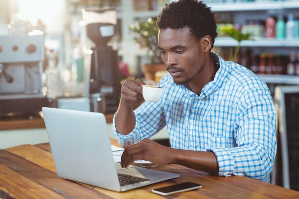 Hombre usando el ordenador portátil mientras toma una taza de café — Foto de Stock