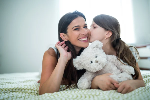 Daughter kissing on mother cheeks on bed — Stockfoto