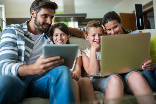 Famille heureuse en utilisant un ordinateur portable et une tablette numérique dans le salon — Photo