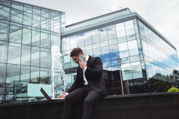 Affärsman med laptop medan du talar i telefon — Stockfoto