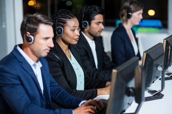 Colegas com fones de ouvido usando o computador no escritório — Fotografia de Stock