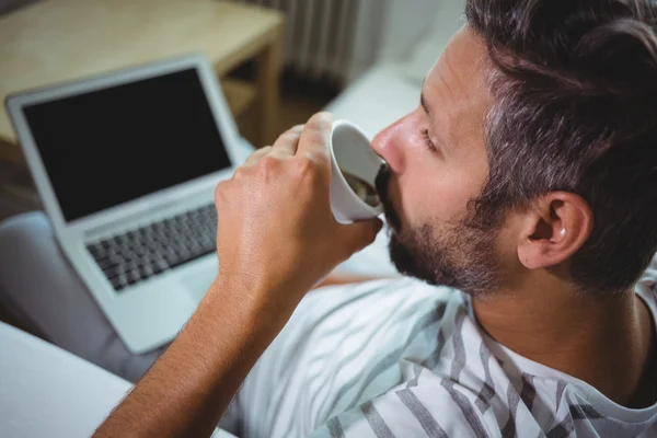 Uomo che prende il caffè mentre usa il computer portatile — Foto Stock