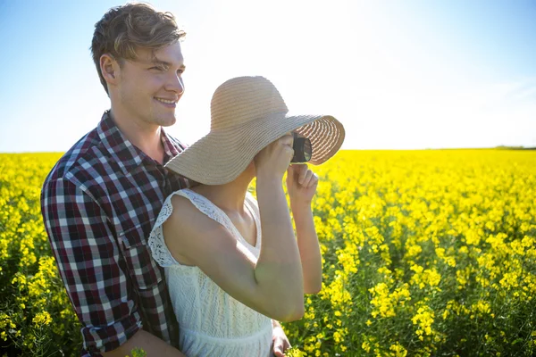 Couple taking picture from camera in mustard field — Stock Photo, Image