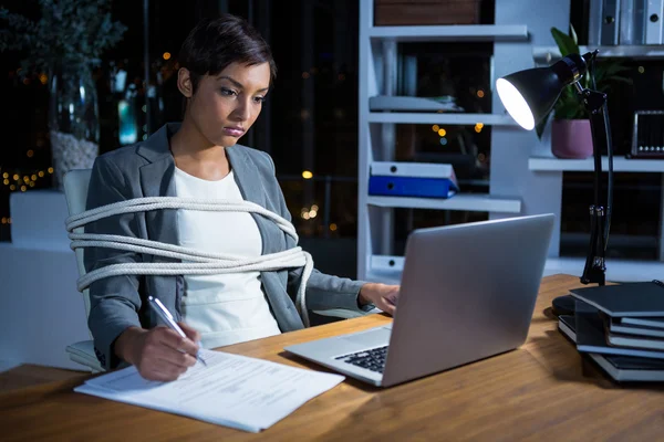 Businesswoman tied with rope while working on laptop — Stock Photo, Image