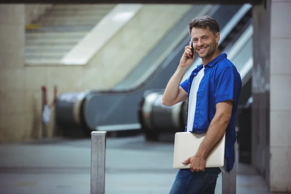 Hombre sosteniendo el ordenador portátil y hablando por teléfono —  Fotos de Stock