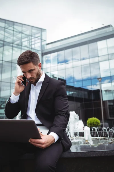 Empresario usando portátil mientras habla por teléfono — Foto de Stock