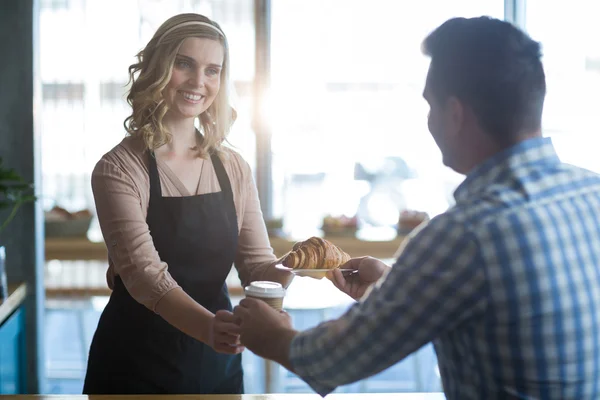 Waitress serving coffee and croissant to customer — Stock Photo, Image