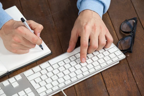 Homem digitando no teclado e escrevendo no diário — Fotografia de Stock