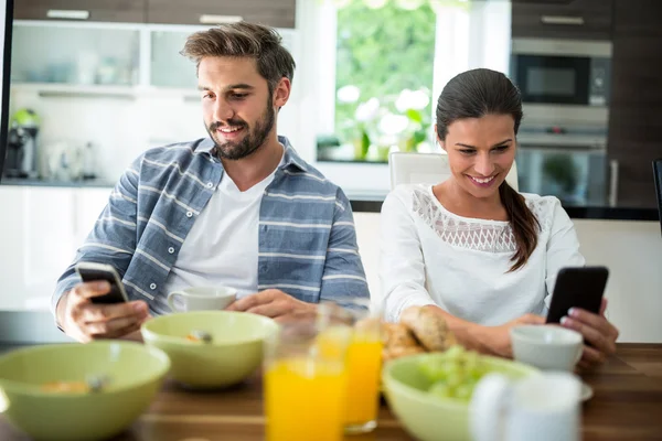 Casal usando telefone celular enquanto toma café da manhã — Fotografia de Stock
