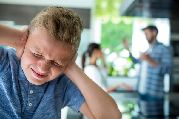 Rapaz triste a tapar os ouvidos enquanto os pais discutem ao fundo — Fotografia de Stock