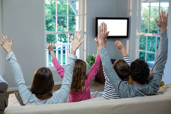Família levantando as mãos enquanto assiste televisão — Fotografia de Stock