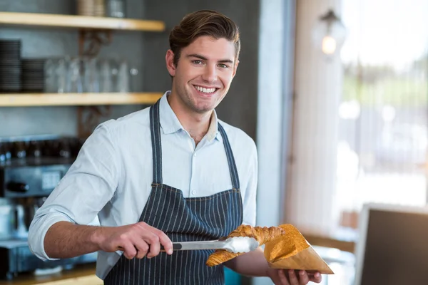 Waiter packing croissant in paper bag — Stock Photo, Image