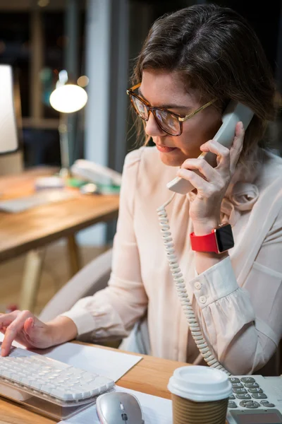 Empresária falando ao telefone enquanto trabalhava no computador — Fotografia de Stock