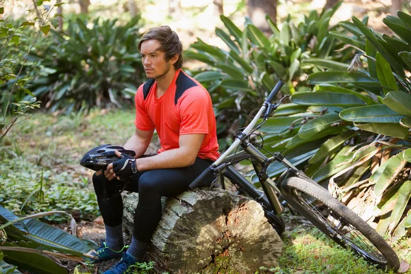 Vélo de montagne mâle épuisé se détendre sur un tronc d'arbre dans la forêt — Photo