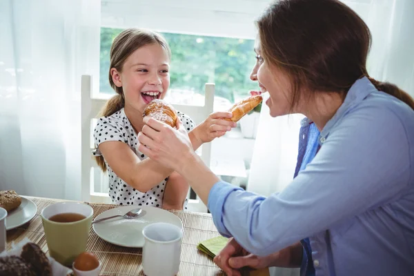 Mother and daughter feeding croissant to each other — Stock fotografie