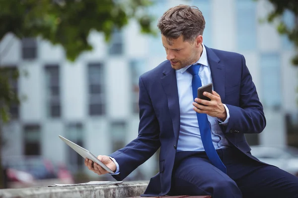 Empresário segurando telefone enquanto estiver usando tablet — Fotografia de Stock