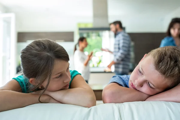 Bambini tristi appoggiati sul divano mentre i genitori litigano sullo sfondo — Foto Stock