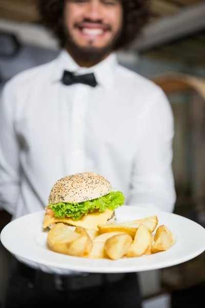 Kellner hält Teller mit Kartoffelchips und Burger — Stockfoto