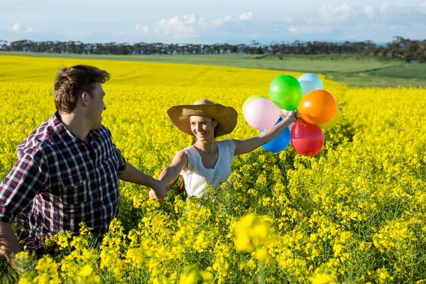 Pareja sosteniendo globos de colores en el campo de mostaza —  Fotos de Stock