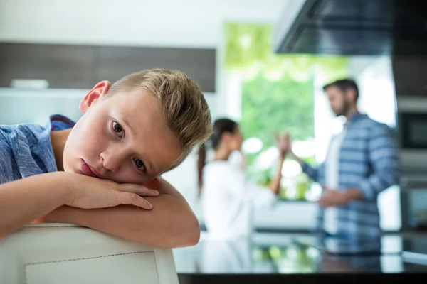 Trieste jongen leunend op de stoel terwijl ouders ruzie op achtergrond — Stockfoto