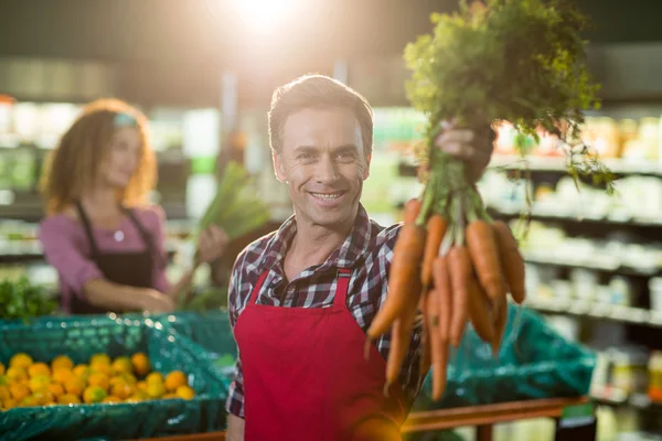 Staff holding bunch of carrots in organic section — Stock Photo, Image