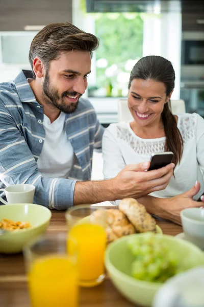 Couple using mobile phone while having breakfast — Stock Photo, Image