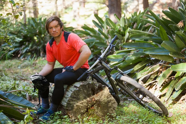Retrato de exausto ciclista de montanha masculino relaxando em um tronco de árvore na floresta — Fotografia de Stock