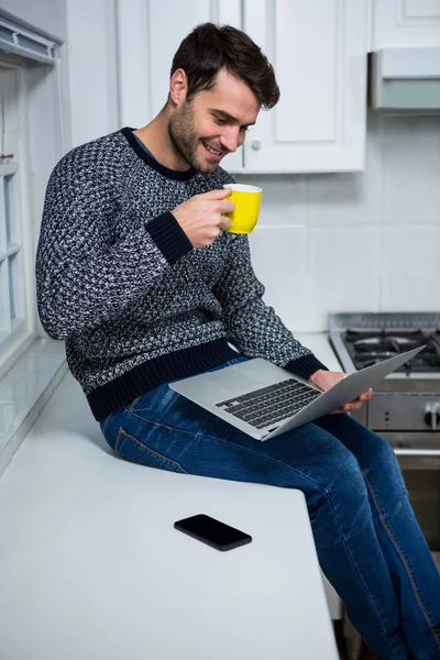 Uomo che utilizza il computer portatile mentre prende il caffè — Foto Stock