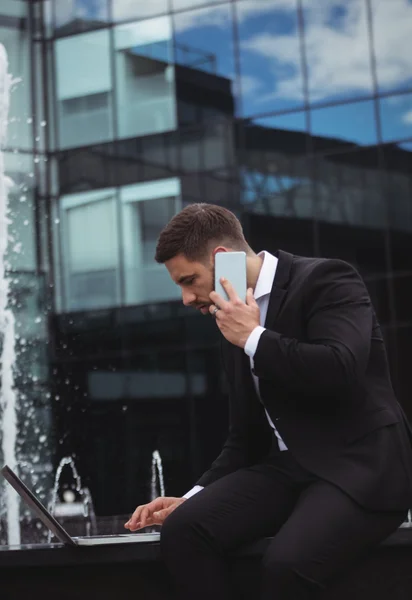 Telefonla konuşurken dizüstü kullanarak iş adamı — Stok fotoğraf