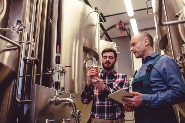 Propietario inspeccionando cerveza con trabajador en cervecería — Foto de Stock