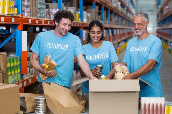 Voluntarios empacando comestibles en caja de cartón — Foto de Stock