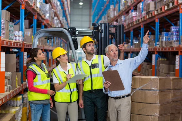 Warehouse manager and co-workers discussing over clipboard — Stock Photo, Image
