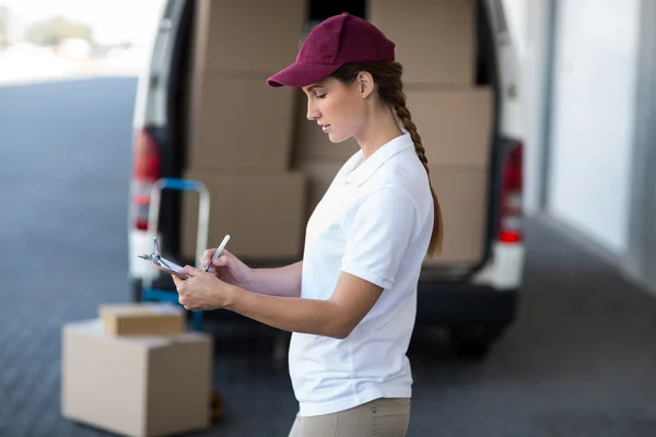 Delivery woman writing on clipboard — Stockfoto