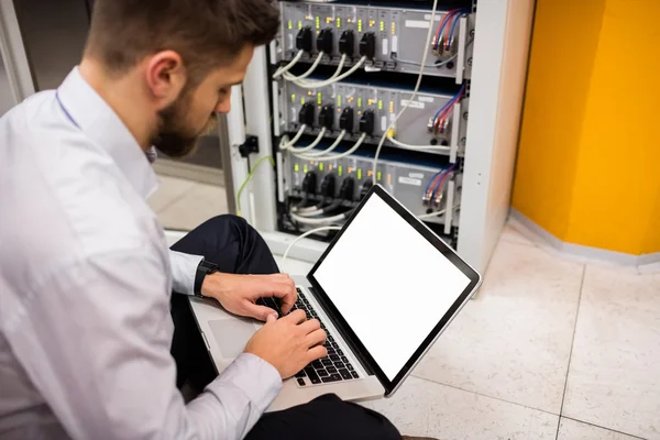 Technician using laptop while analyzing server — Stock fotografie