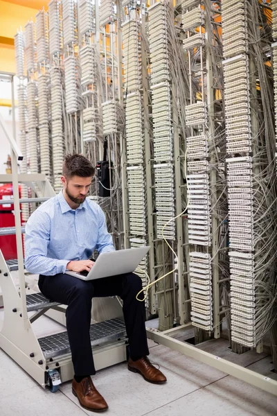 Technician using laptop while analyzing server — Stock fotografie