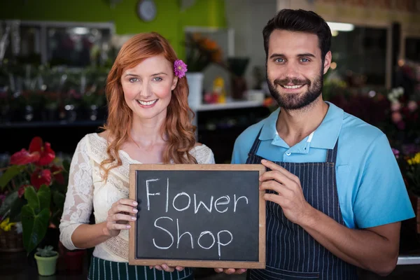 Paar holding leisteen met bloemenwinkel ondertekenen — Stockfoto